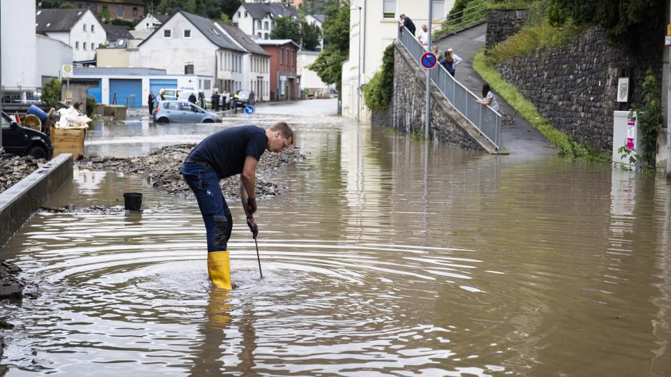 Junger Mann steht bis zu den Waden auf einer überschwemmten Straße.